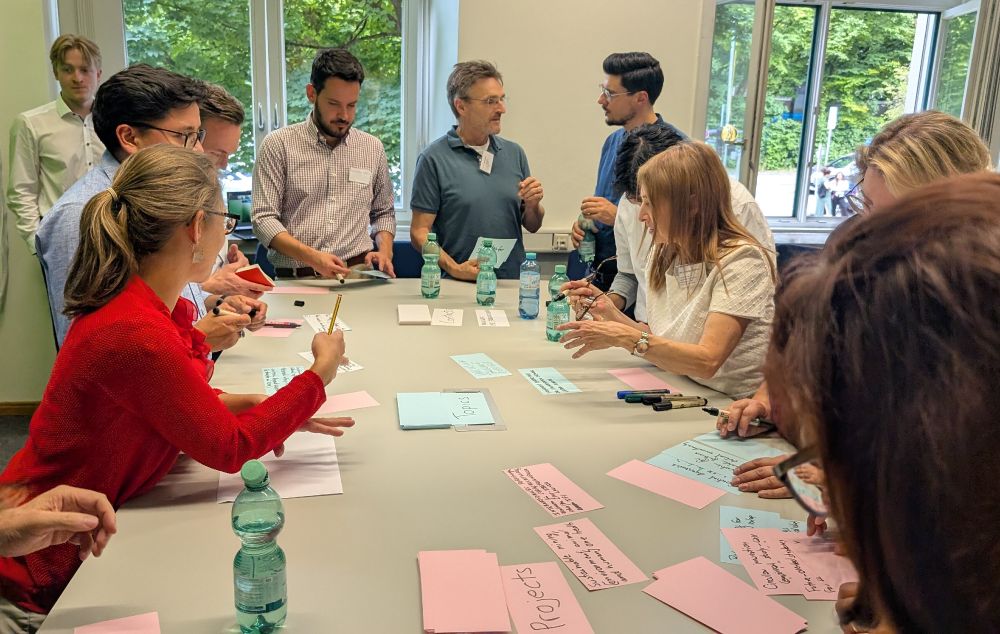 The participants are standing around a large table, writing short info on red, blue and white memo cards. They are collecting valuable contacts, potential topics to explore around sustainability transitions, and current and planned projects that might align with the GIST-Hub. 