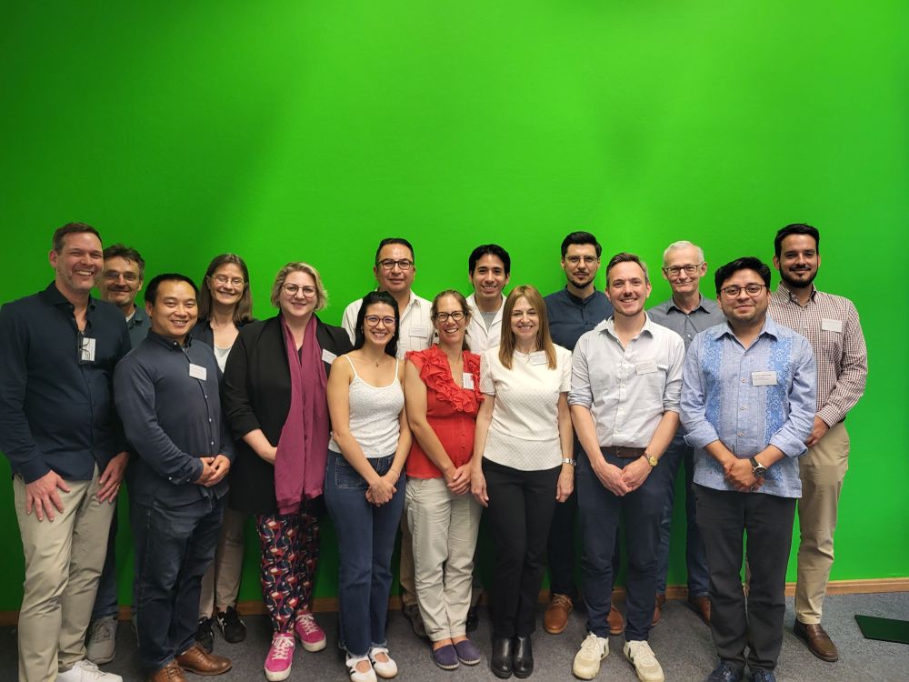 A group picture of the participants. They are standing in front of a bright green wall that usually serves as a green screen. 