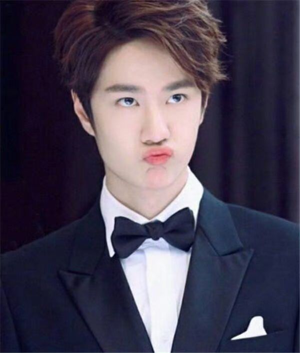 Full on pursed lips pout wearing a black suit with white shirt and black bow tie 