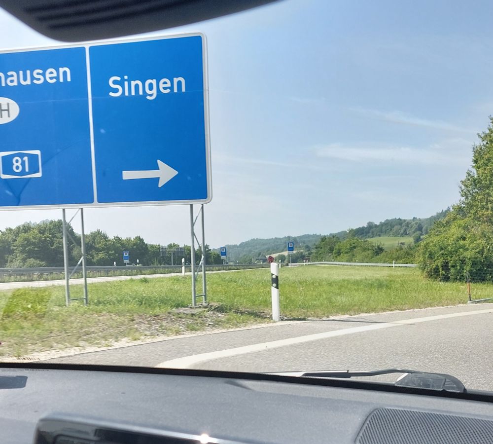 A large Autobahn road sign pointing to the city of "Singen", which also happens to mean "to sing".