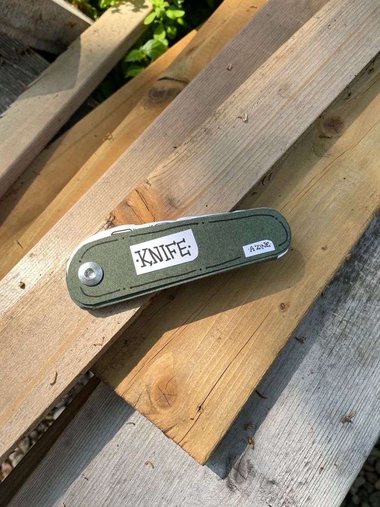 a green booklet shaped like a knife against a background of wood planks
