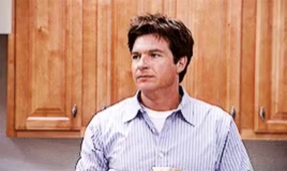 a man in a striped shirt is sitting in a kitchen with a cup of coffee in his hand .