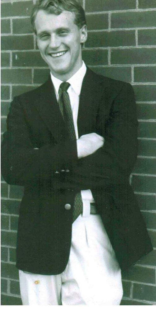 A black and white photo of the author as a grinning, feckless 21-year-old. Wearing tie and jacket and khakis, arms crossed, leaning up against a brick wall.