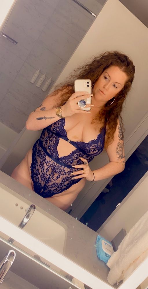 Shea taking a mirror selfie, in a dark blue lace teddy. 