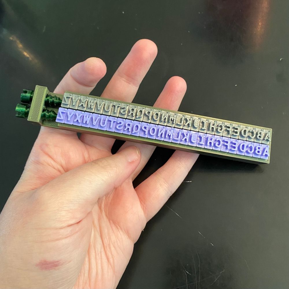 Photo of a test print of only two lines of movable type, each line the 26-letter alphabet, with 3D printed screws holding them in place at the end.