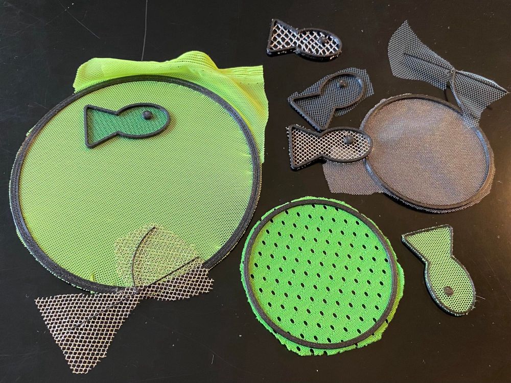 Photo of various little print tests on meshes and tulles: hoops and little fish shapes, mostly neon yellow/green and metallics.