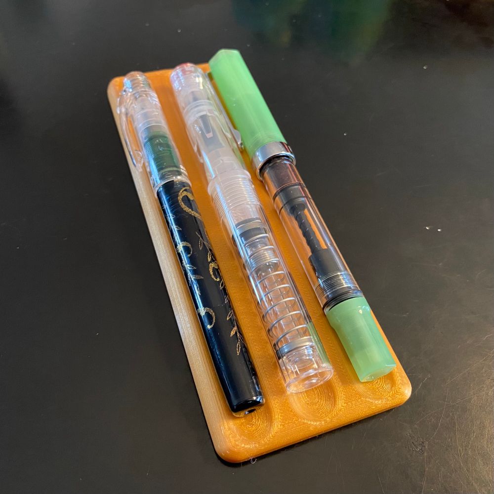 Photo of a 3D printed fountain pen rest with with three fountain pens on it.