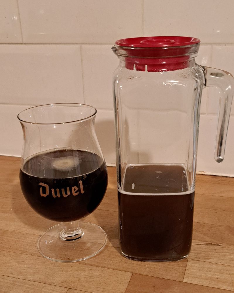 A large glass jar with a red plastic lid. It holds a brown liquid, it's wort and mixed yeasts. There's a Duvel glass holding beer next to the jar. This is my kitchen.