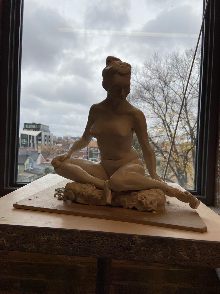 Clay sculpture of a woman sitting down with her head tilted down