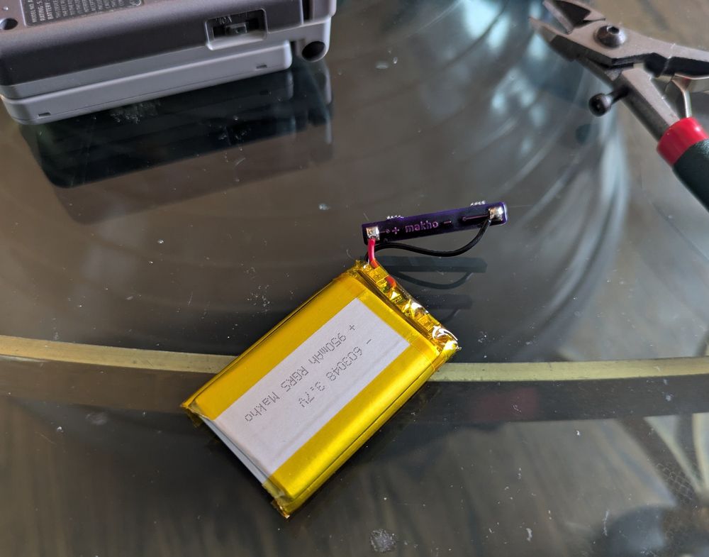 Photo of a flat, wrapped lithium ion battery, the wires coming out of it have been trimmed and soldered to a small pcb