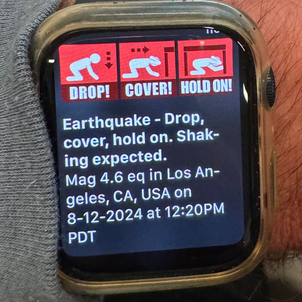 Apple Watch displaying "DROP! COVER! HOLD! Earthquake - Drop, cover, hold on. Shaking expected. Mag 4.6 eq in Los Angeles, CA, USA on 8-12-2024 at 12:20PM PDT"
