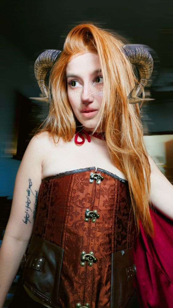 Fawn creature with long ginger hair, ram horns, a velvet burgundy cape wearing a brown brocade corset, more intense makeup editing (creepy Ed)