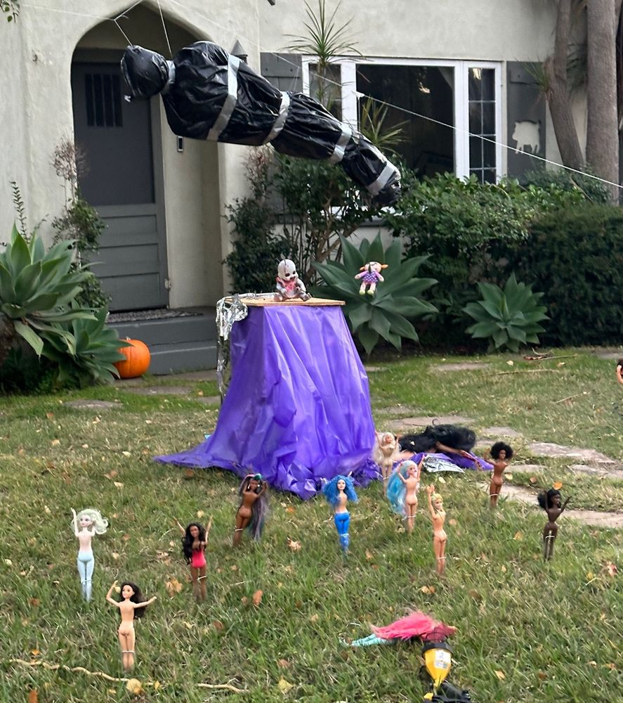 pic from the quoted post where there are a bunch of barbie-sized dolls in various states of undress standing with their arms raised under a hanging wrapped-up body