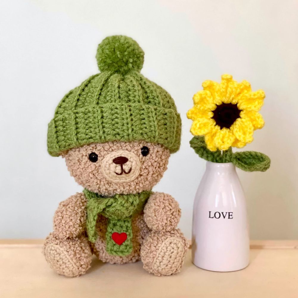 Teddy bear with a crocheted sunflower in a vase with the word “love”
