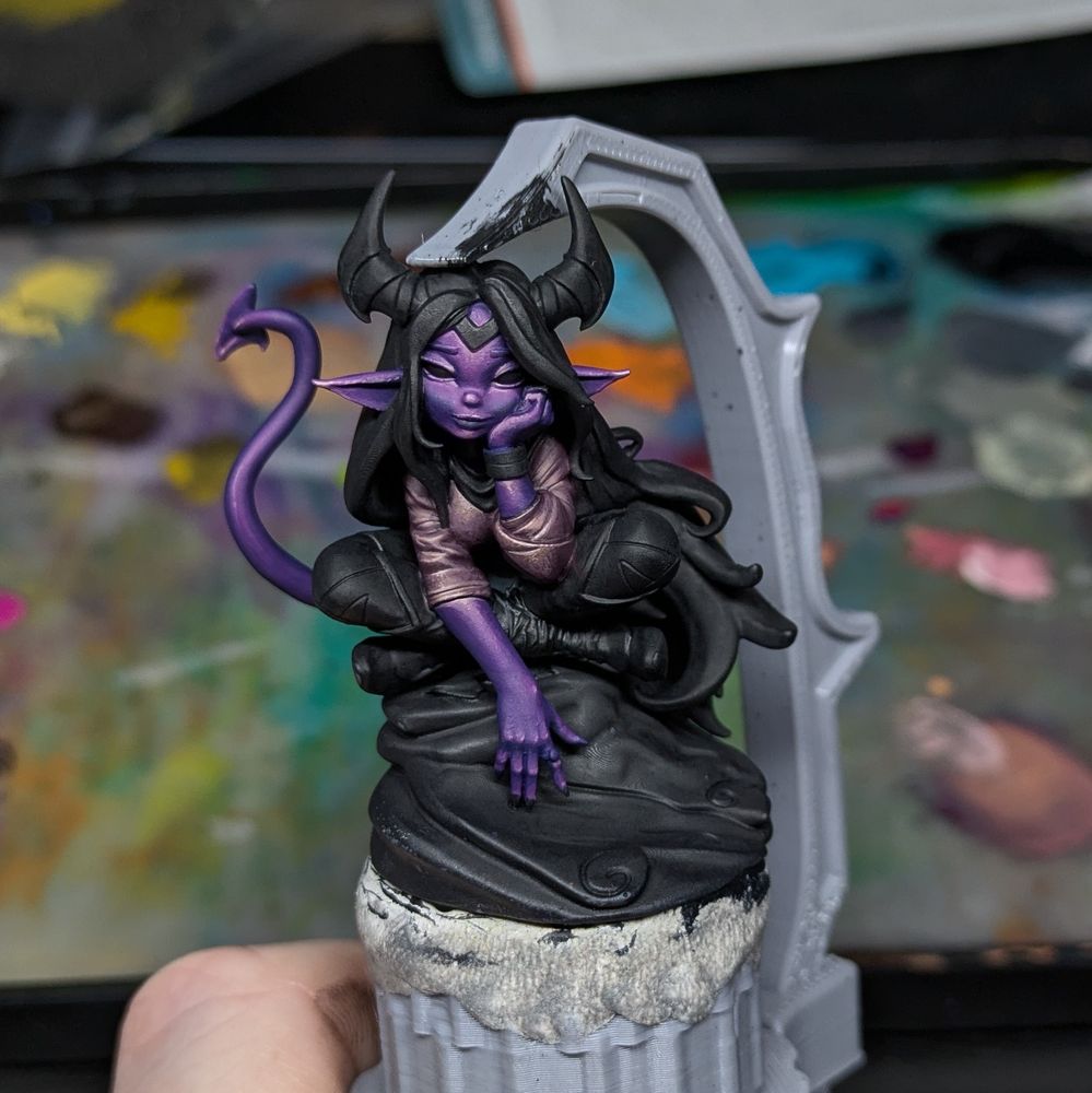 A half finished mini of a tiefling girl sat on a rock