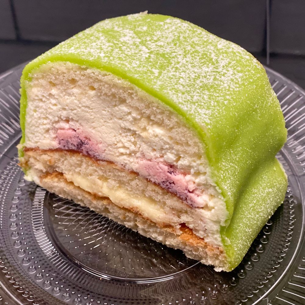 Closeup of a prinsesstårta. Soft layered cake with raspberry, whipped cream and marzipan filling. A green coloured marzipan layer covers it. 