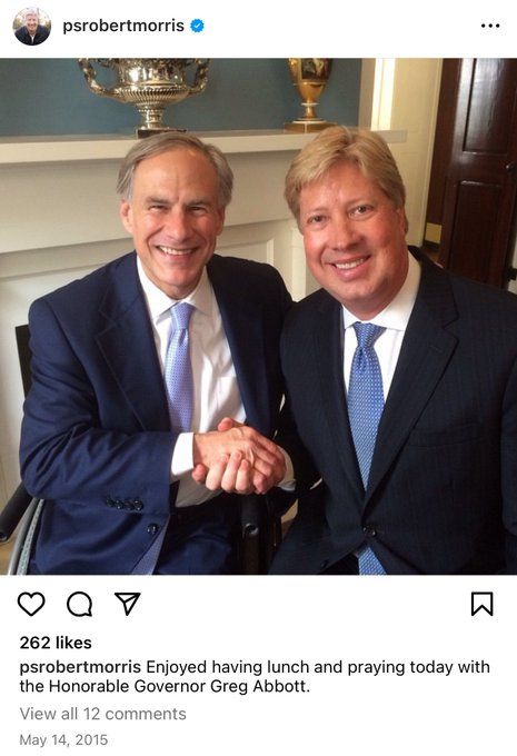 Greg Abbott and Morris in formal attire shaking hands, seated in a well-decorated room with a trophy and a wooden cabinet in the background.