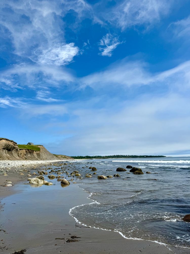 photo of an Atlantic ocean beach in Nova Scotia. Houses sit atop the cliff overlooking the beach. 