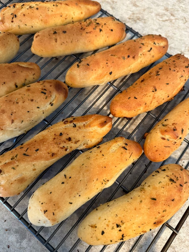 Nine golden brown garlic breadsticks sitting on a cooking rack. 