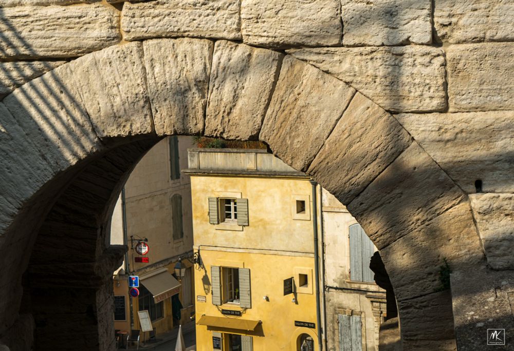 Color photo of the view looking through a stone arch at old buildings beyond.