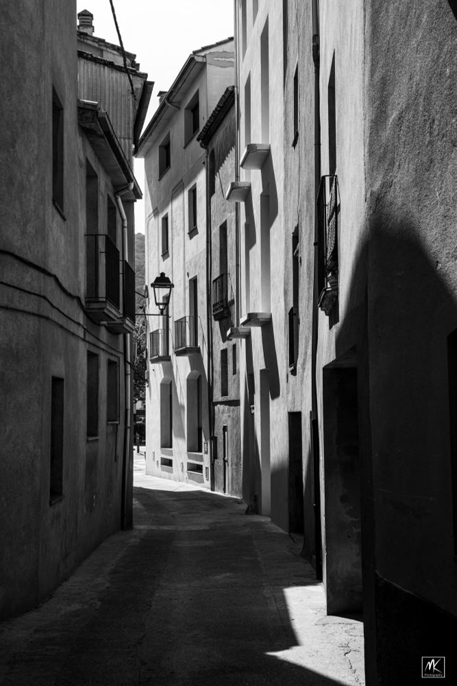 Black and white photo of buildings and sunlight along a curved, narrow street.