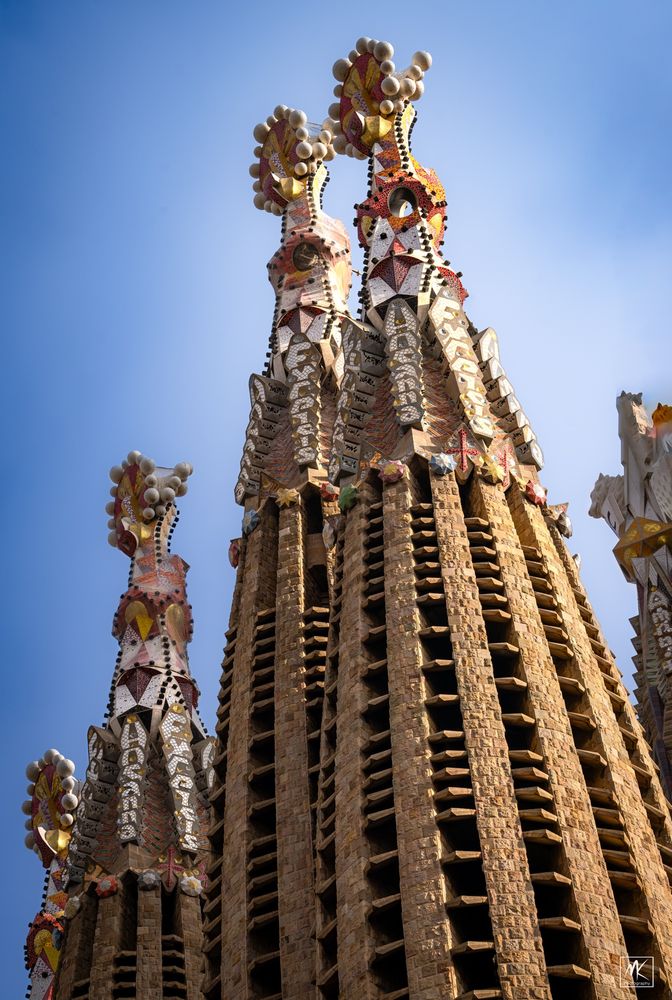 Color photo of the pointed tops of several conical towers of the Sagrada Família Basilica, capped by colorful tile mosaic-covered abstract forms 