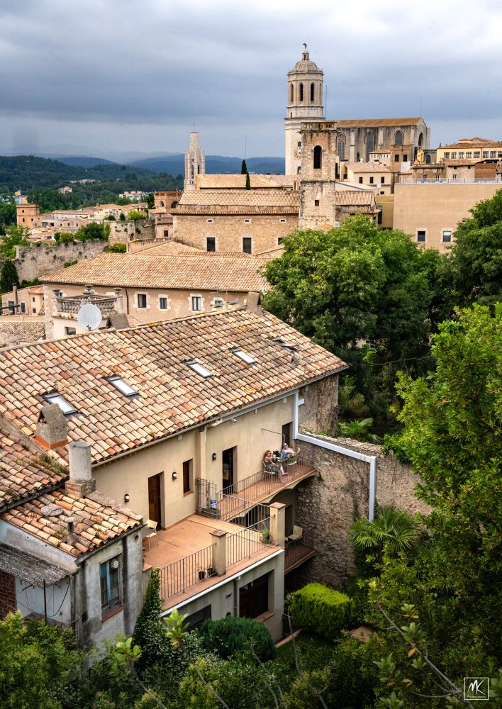 Color photo looking out over a city with tile roofed buildings and the tower of a cathedral in the background. 