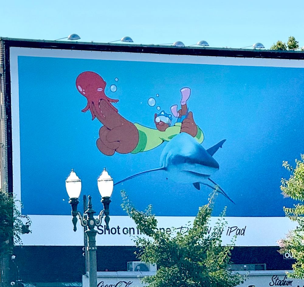 Photo of an Apple billboard with a drawing of a person with a small octopus on their finger, over a photo of a shark 