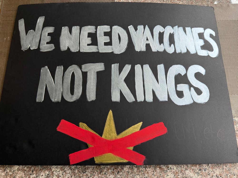 Protest sign reading we need vaccines not kings with a gold crown covered by a red x.