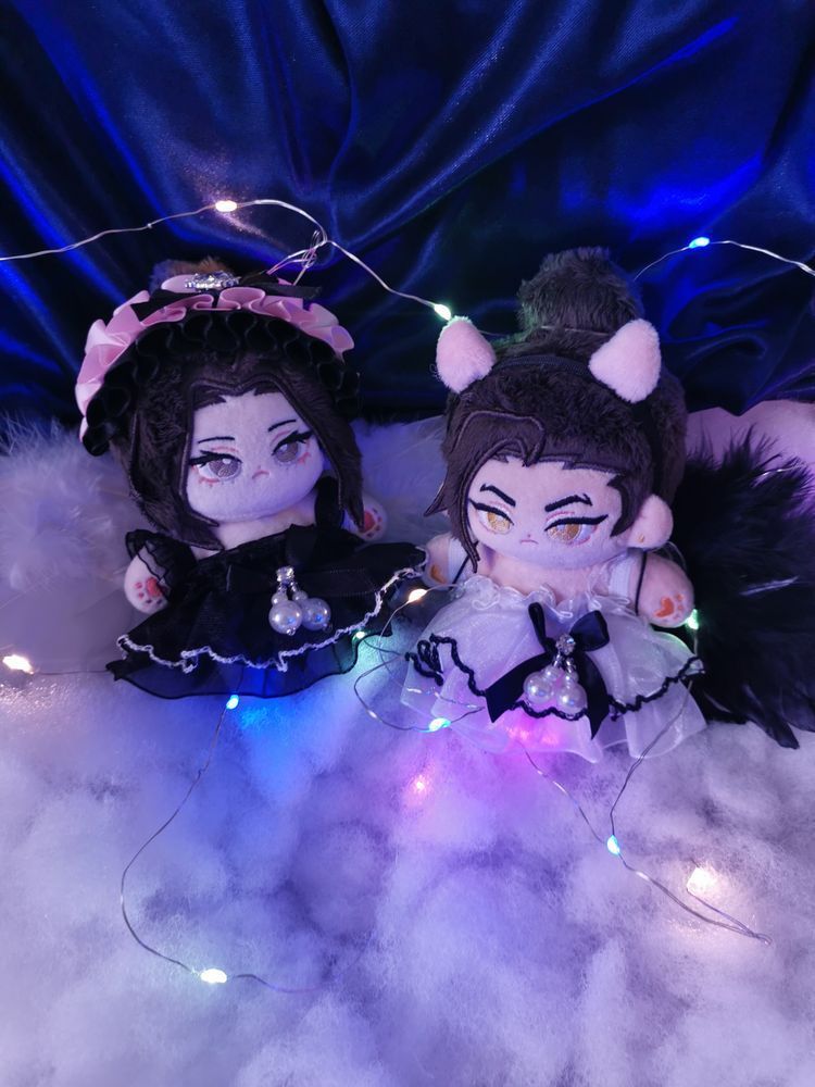 Fengqing dolls are in the middle of the photo. The background is dark blue and the dolls are sitting on "clouds" (poly fill). Mu Qing, on the left, is dressed in a black dress, has a black and pink head band, and white wings. Feng Xin is wearing a matching white dress, with devil horns and black wings. Around them are small, multi coloured fairy lights