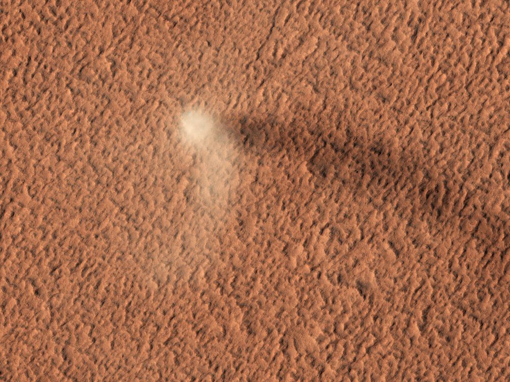 Image shows a dust devil in action, with a dark streak behind the puffy cloud as it travels across a relatively flat landscape on Mars. (NASA/JPL-Caltech/University of Arizona)