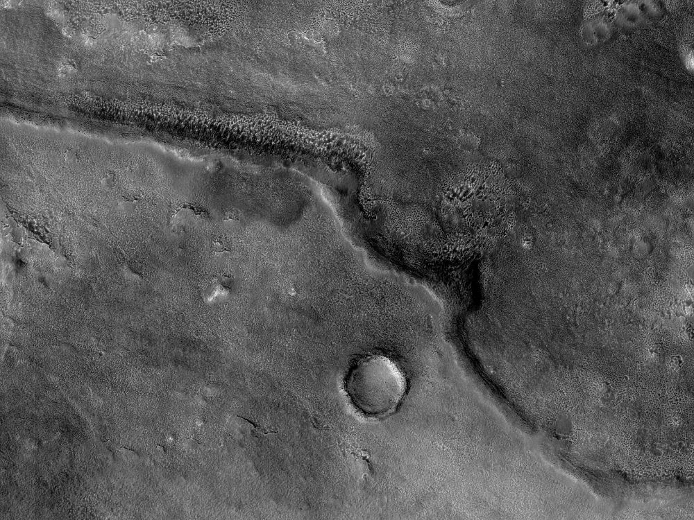 Image shows a long ridge extending from one side of the scene to the other. There is also an old impact crater in one section of the picture. (NASA/JPL-Caltech/University of Arizona)