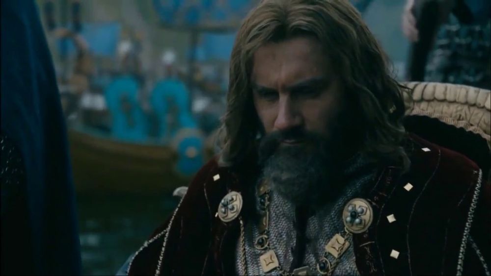 Rollo close up on a boat in fine french garb with gold clasps long hair and beard.
