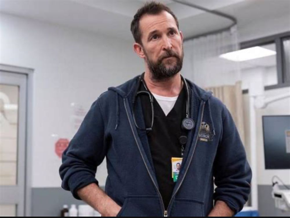 Bearded man with his hand in the pockets in hooded jacket with stethascope around his neck.