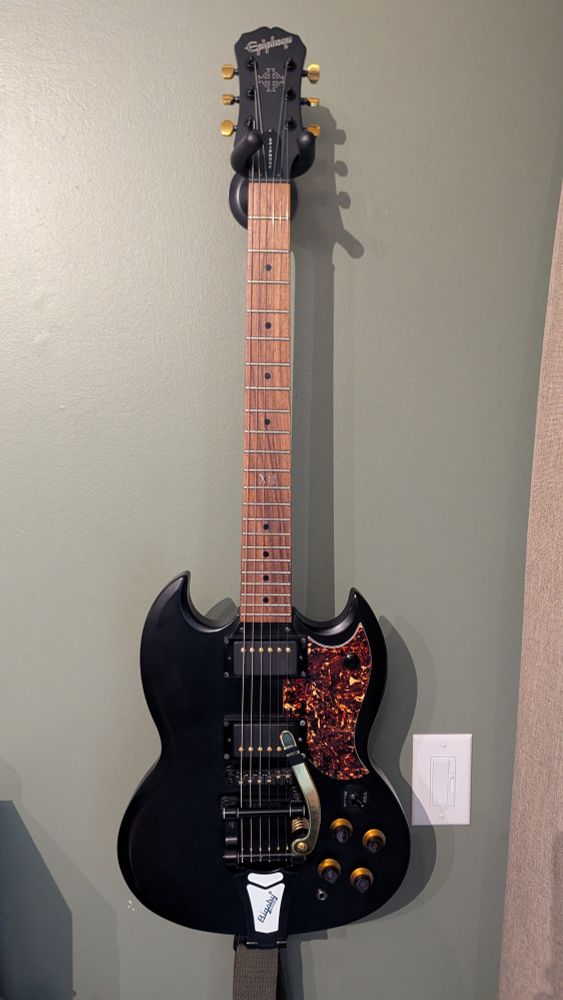 A black Epiphone SG with tortoise shell pick guard and a Bigsby tremblo