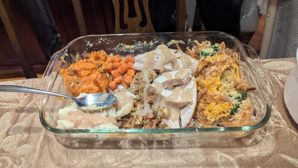 A large Corningware dish filled with turkey, stuffing, candied yams, mashed potatoes, gravy and some cheesy broccoli 