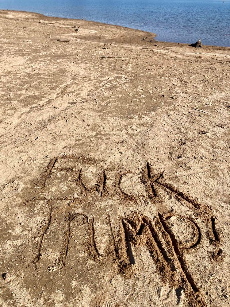 The wise phrase Fuck Trump scratched into the sand at a lake. 
