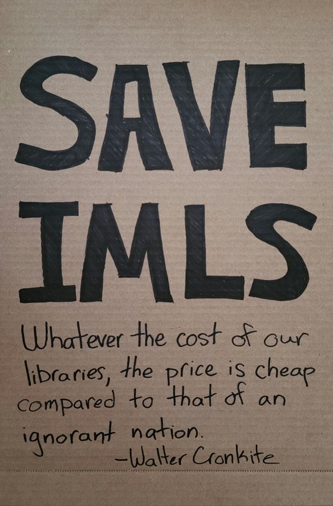 Hands Off cardboard sign that reads "save imls. Whatever the cost of our libraries, the price is cheap compared to that of an ignorant nation." Walter Cronkite