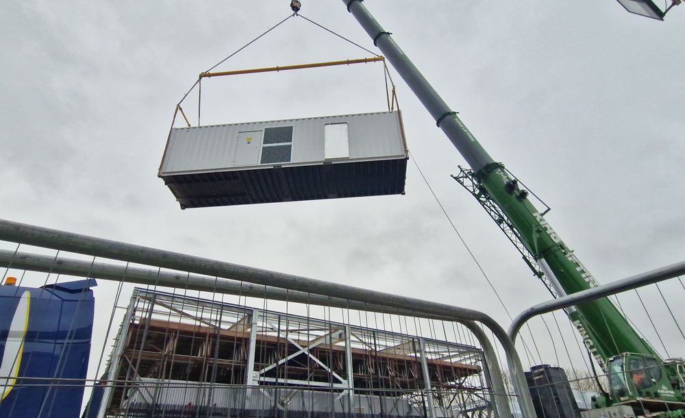 A crane is lifting a section of the Isambard-AI supercomputer into the air. 