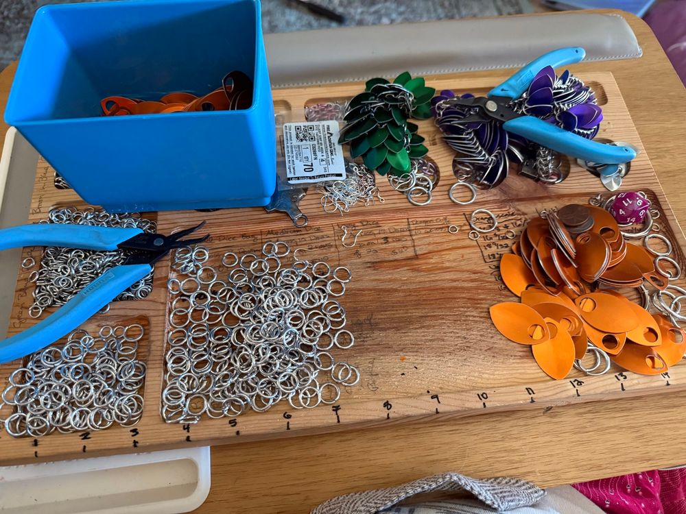 Photo of a scalemaille work mat with silver rings, blue pliers, and orange scales 