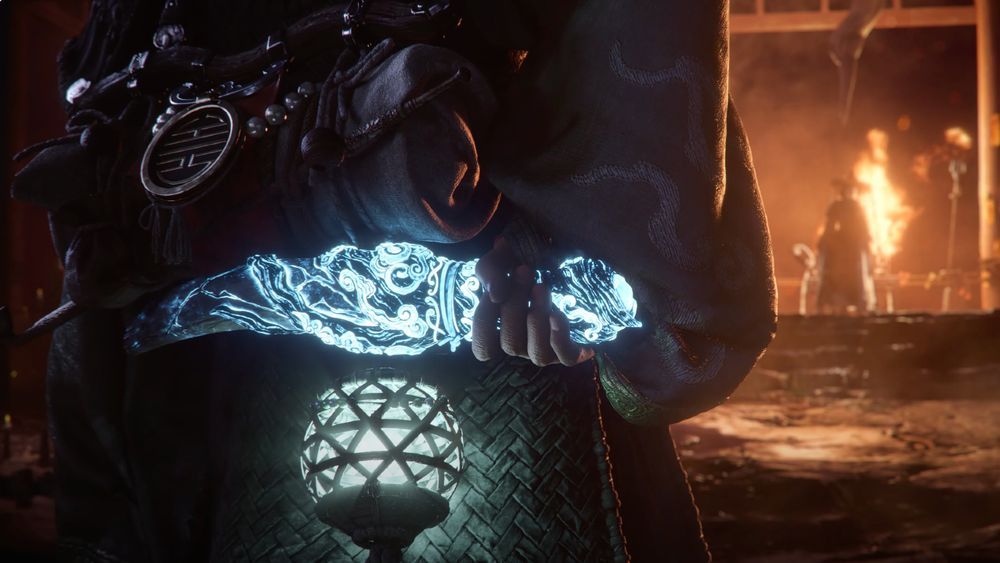 A screenshot from the Woochi the Wayfarer reveal trailer showing the back of the protagonist with a teal orb lit up while holding a girthy blade, lit in neon light blue. In the background, ahead of the protagonist, is a large fire with a shaman woman standing in front of it menacingly. 
