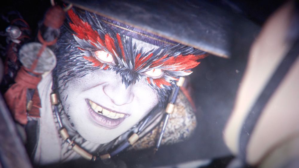 A menacing face from the reveal trailer of Woochi the Wayfarer. It is bathed in bright white light with dinosaur-like scales and feathers adorning the top of the nose and area surrounding the character's eyes. 