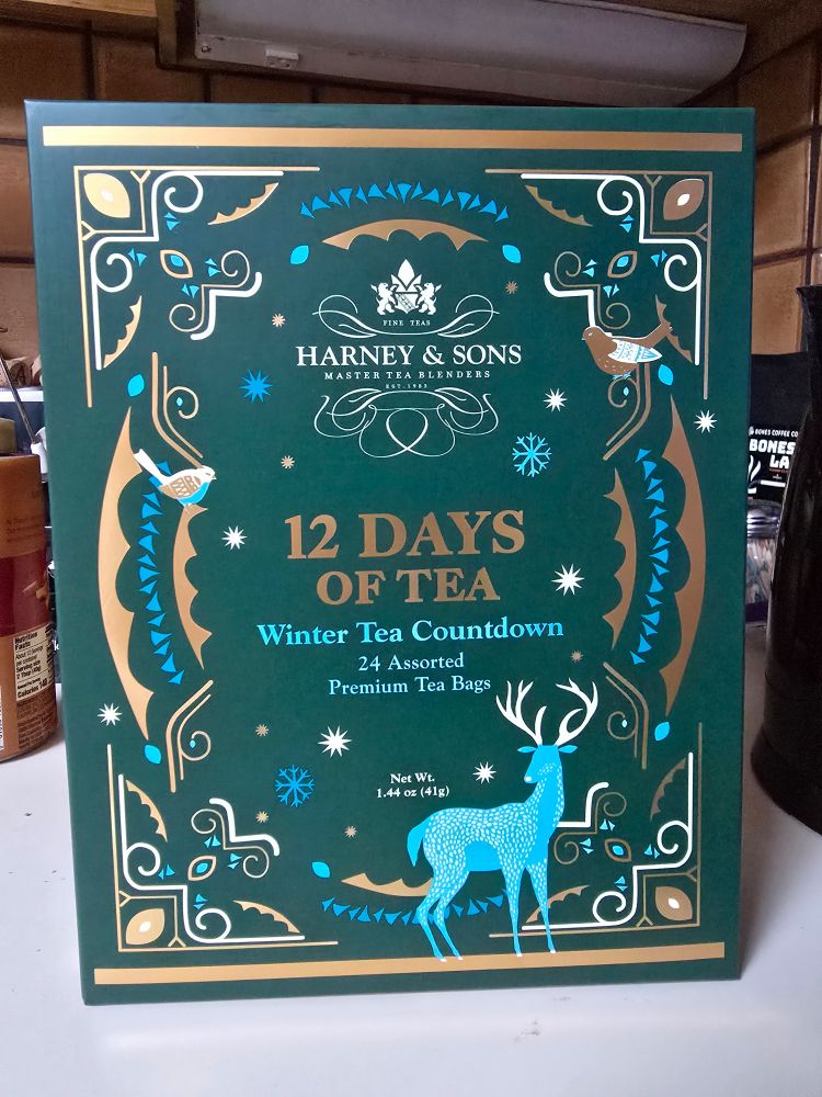 Closeup of the front of the box of Harney Tea's 12 Teas Of Christmas Advent Calendar. It depicts a stylized reindeer and birds against a green abstract backdrop. No tea is illustrated, oddly