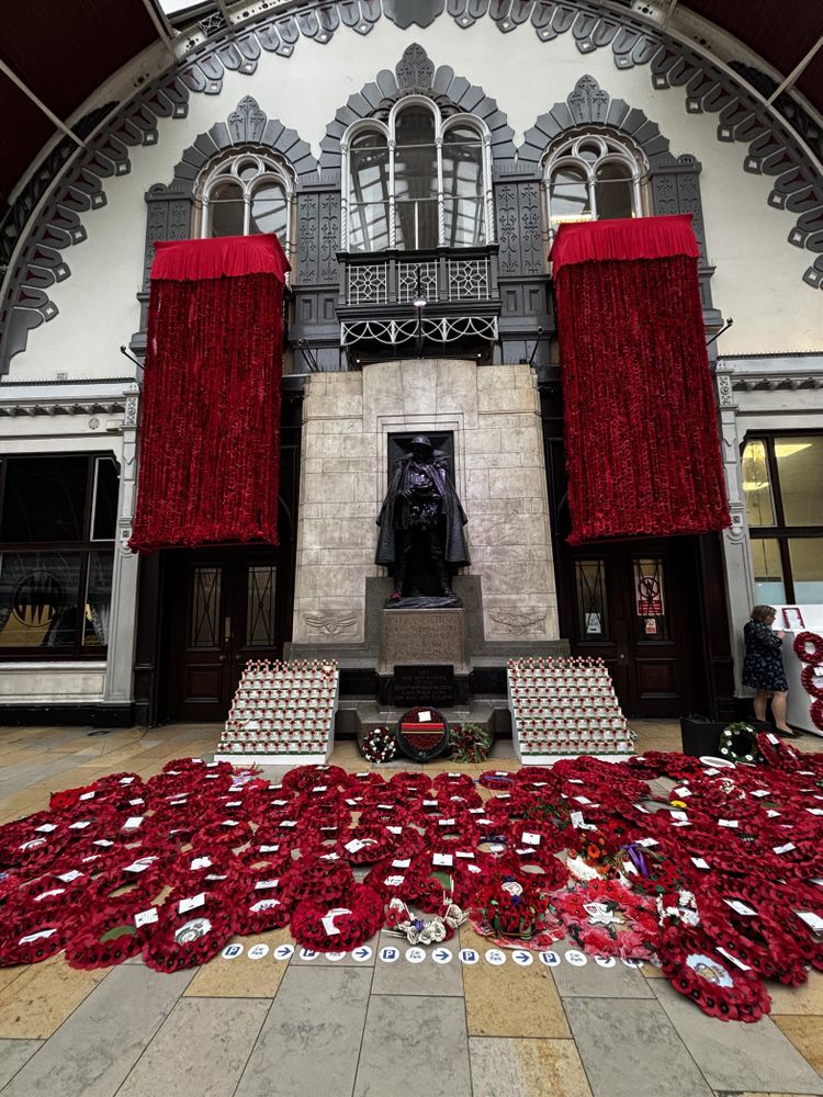 The war memorial statues shrouded by hanging poppy curtain and along the floor, poppy wreaths laid in front of the memorial 