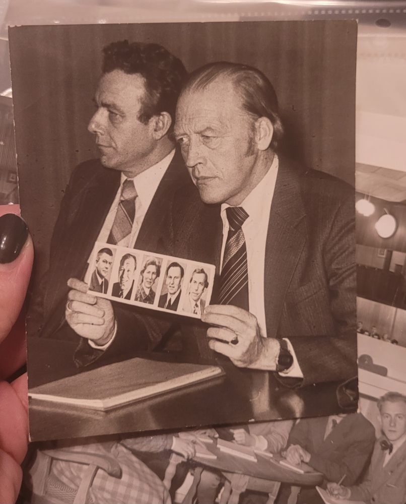 Oddvar Nordli holder opp et bilde med fem små portrettbilder på. Pappa er der, men det er muligens også den atale røtta Ronald Bye. I bakgrunnen sitter Reiulf Steen. 