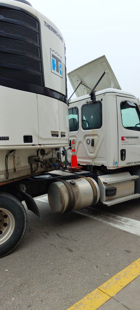 A cone riding between the cab & trailer of a white refrigerated semi truck