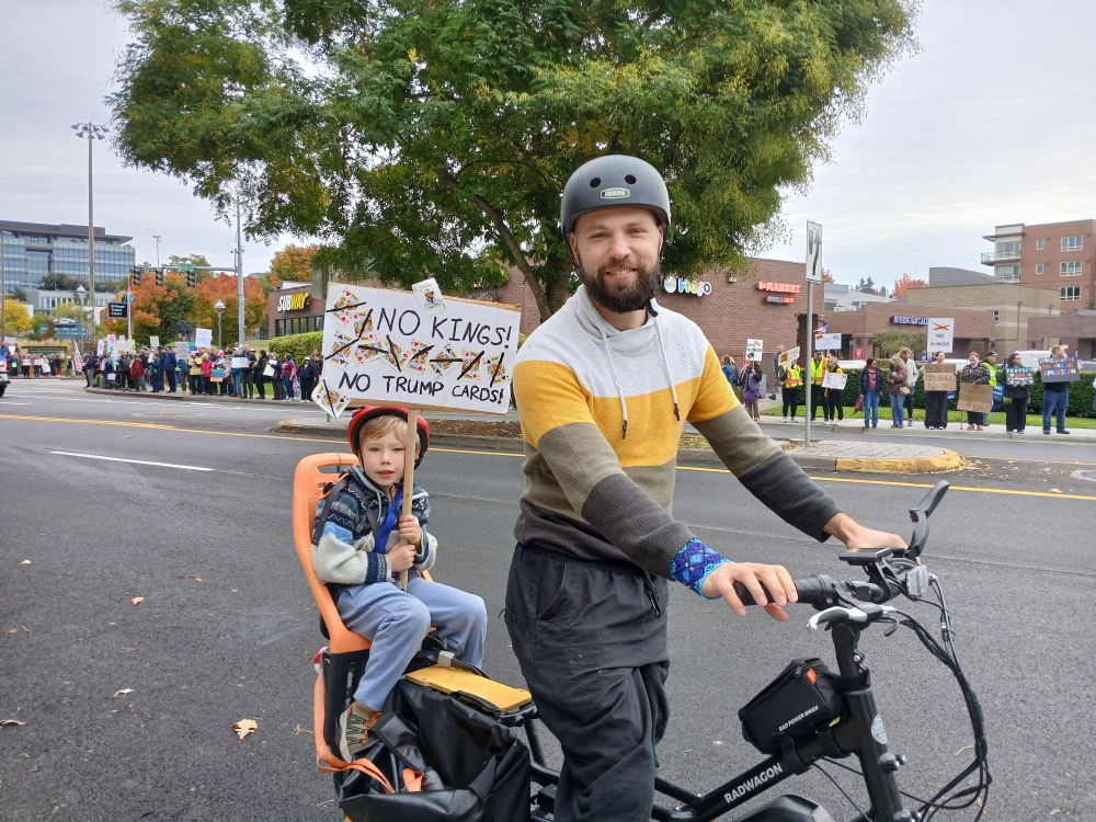 Dad and kid with No Kings sign on bike