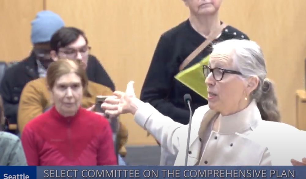 A woman with her arms up in a "sorry" gesture at the microphone