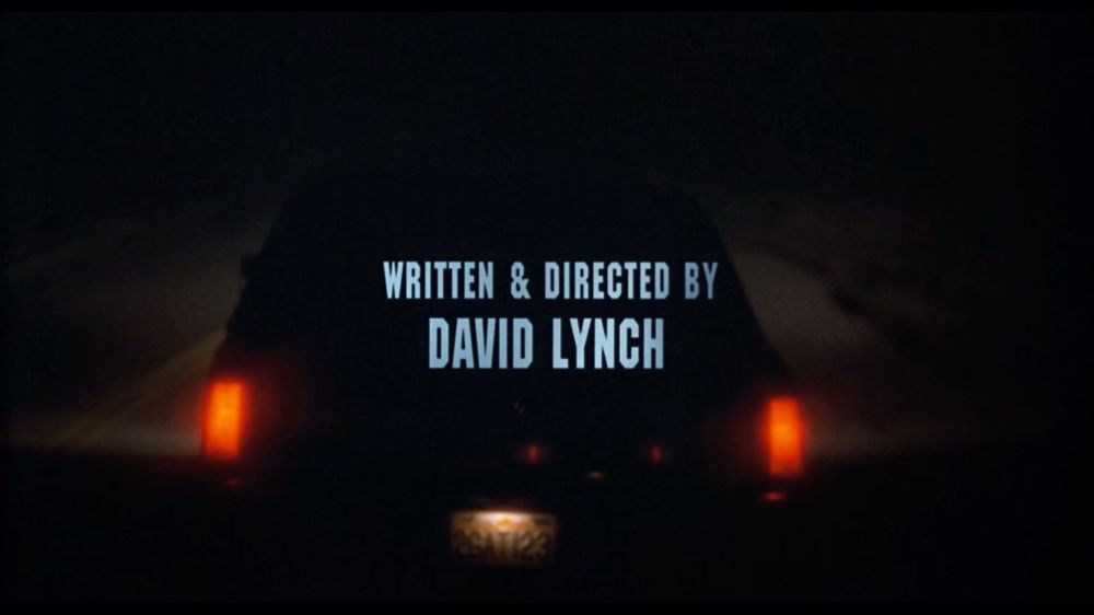 The back of a car at night with its lights on. 
In the middle is a text « written & directed by David Lynch »