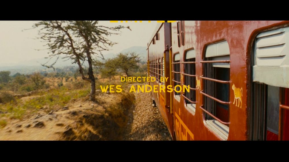 Screenshot from The Darjeeling Limited. 

A red train is on the right side of the picture. The train is riding in a deserted landscape with a tree. 
In the middle, in yeallow letters, it says : Directed by Wes Anderson
